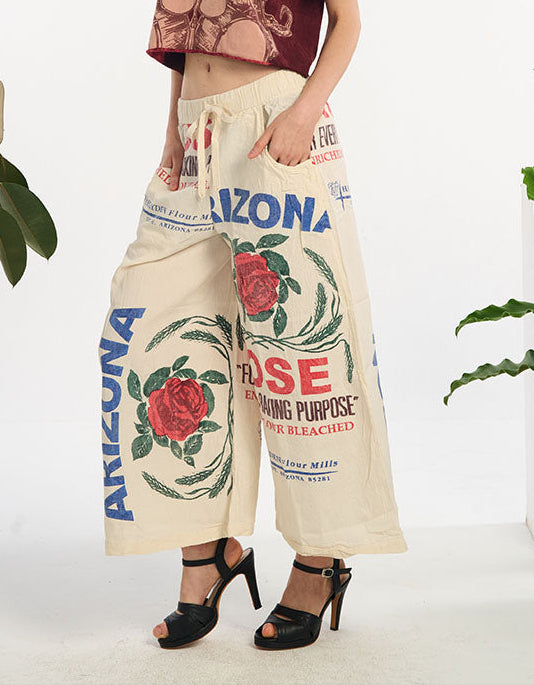 Person wearing cream-colored pants with rose and arizona rose feedsack design, standing against a white background.