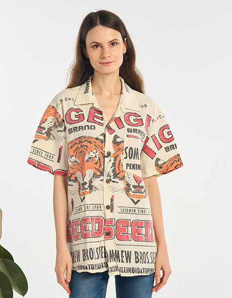 Woman wearing a colorful tiger shirt and blue jeans standing in a room with plants.