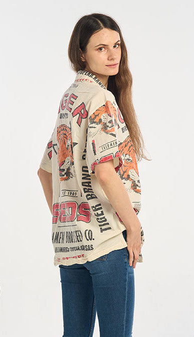 Woman wearing a tiger shirt and blue jeans standing in a room with plants.